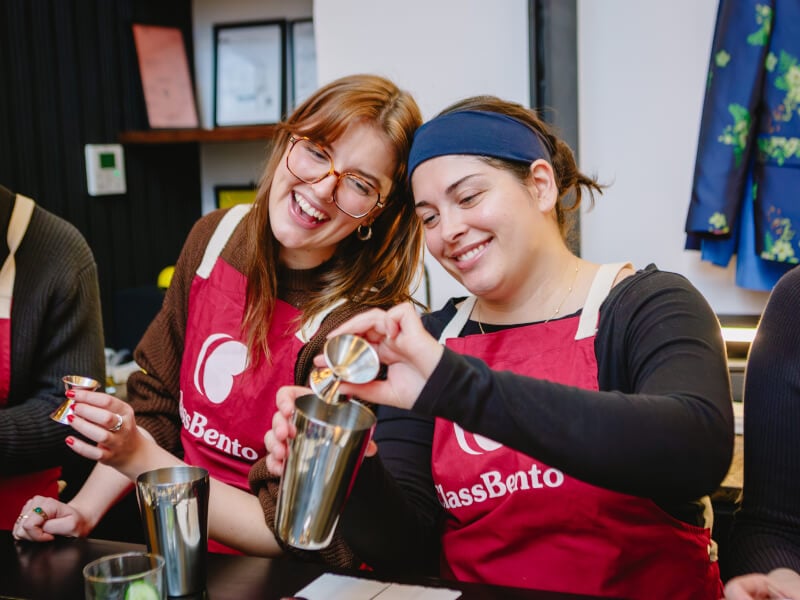 Two people smiling while making cocktails together